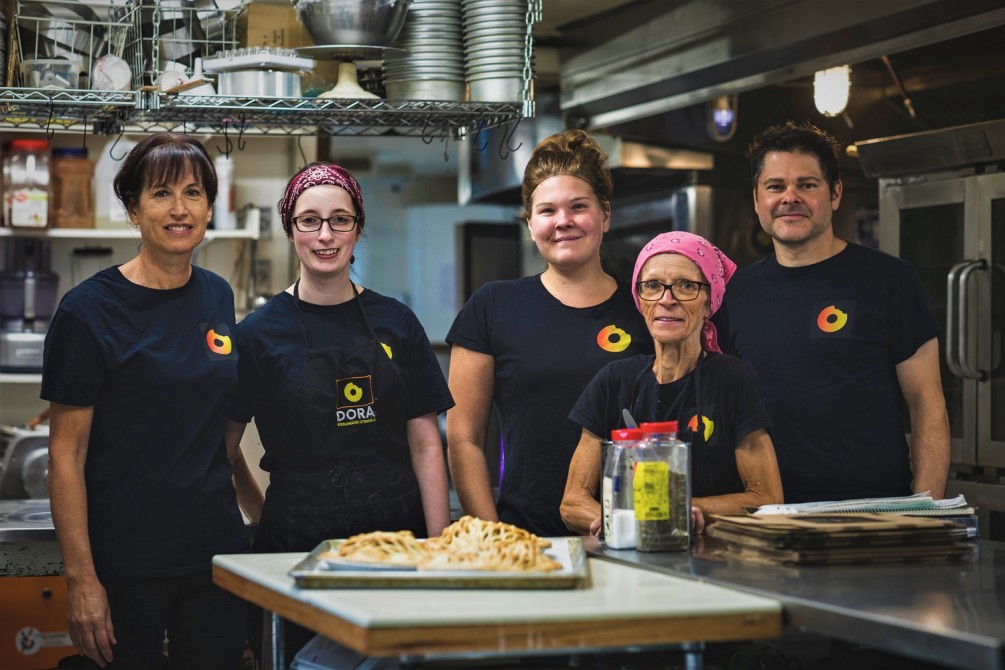 L'équipe Dora: L'équipe Dora est comprise d'une douzaine d'employés - un petit groupe est produit sur la photo, dont la chef beignère, la chef pâtissière, la chef de cuisine et le propriétaire.